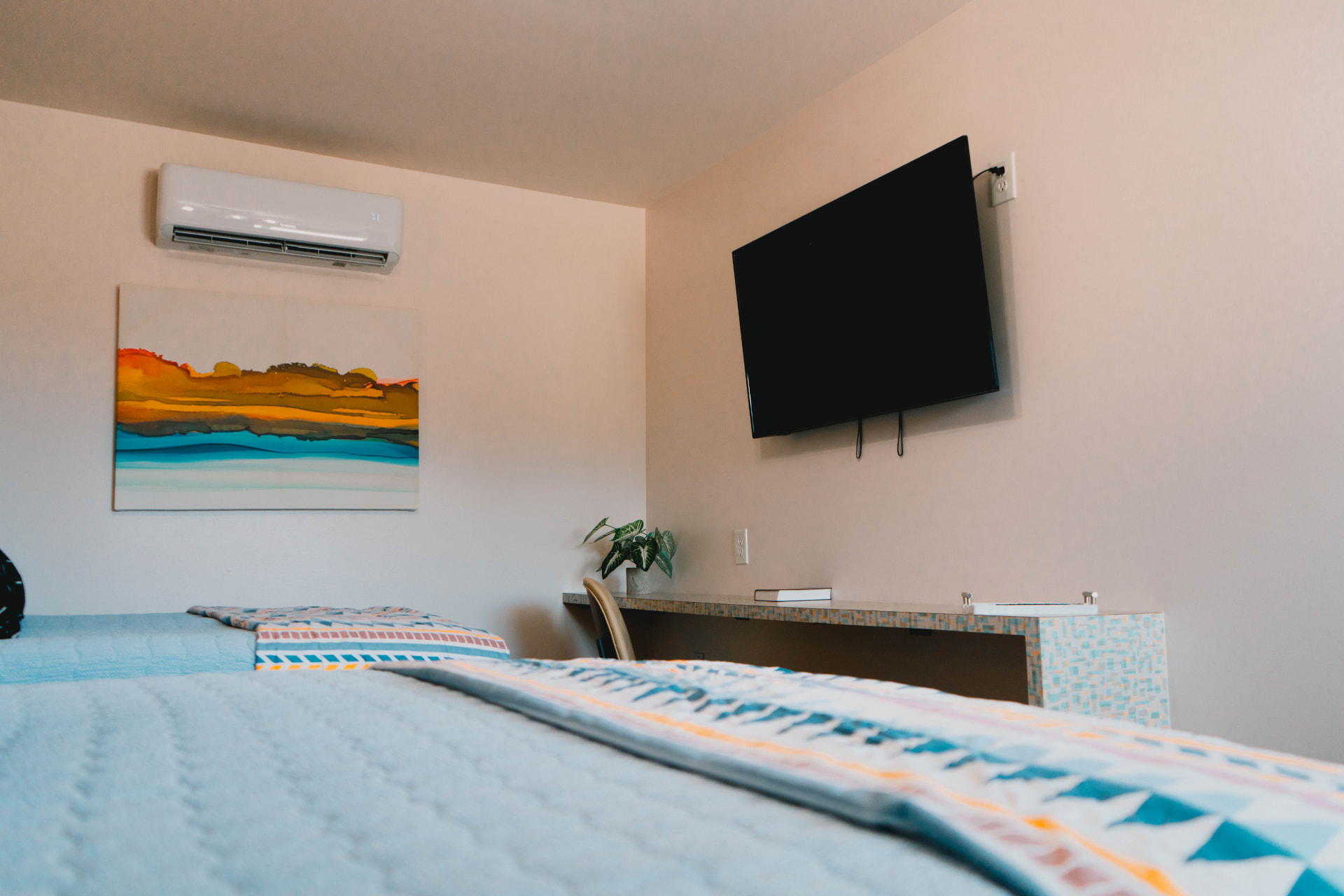 Guest room with a wall-mounted TV, desk, and colorful artwork