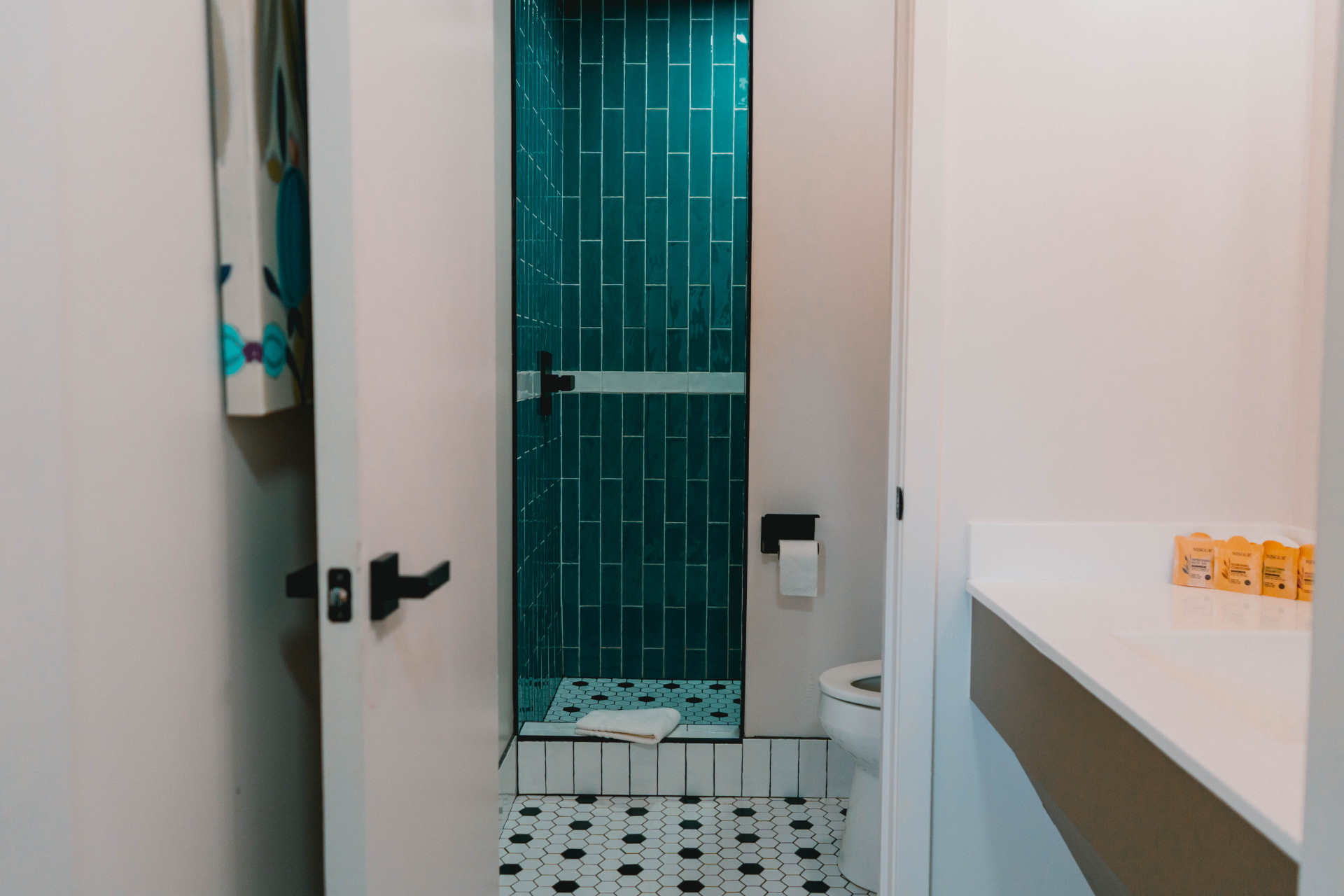 Guest bathroom with a teal-tiled walk-in shower and patterned floor