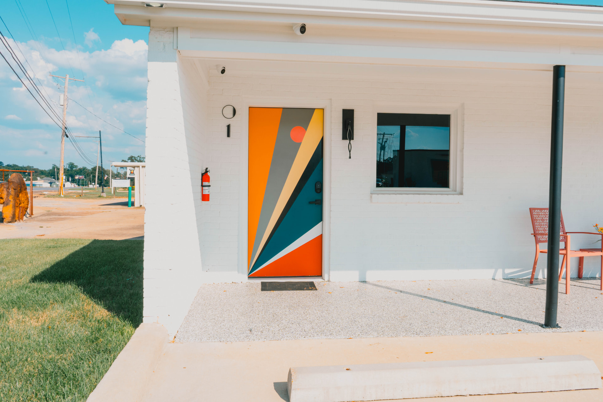 Room one with a sunburst-painted door beside a shaded walkway