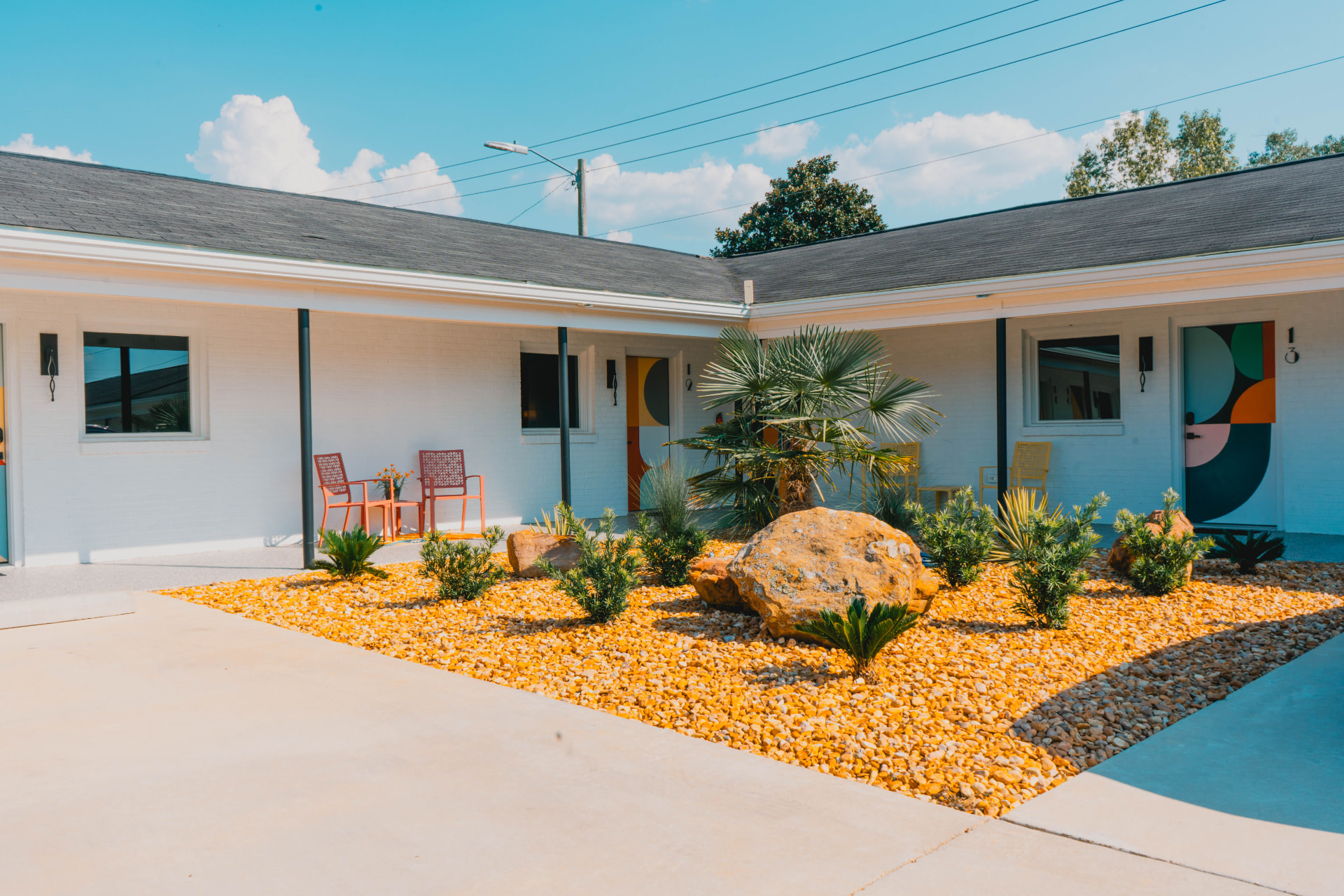 Sunny courtyard with patterned guest doors, patio chairs, and desert landscaping